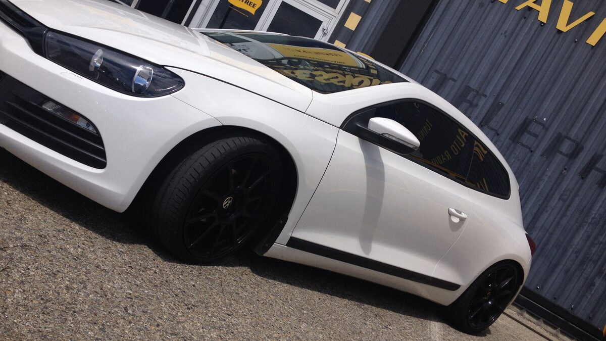Volkswagen Scirocco blanche aux vitres arrière teintées devant l'atelier d'Orange
